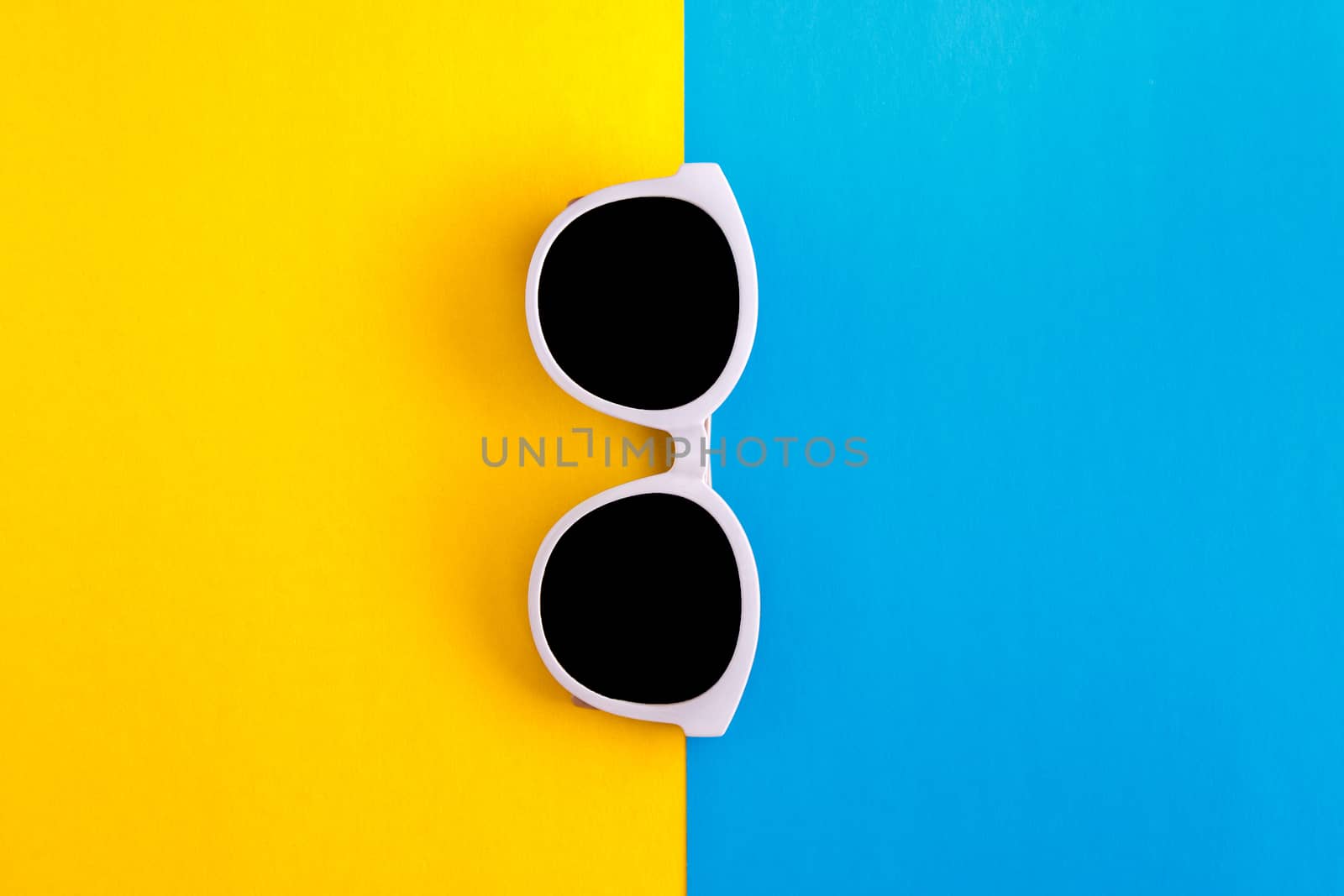 Sunny stylish white sunglasses on a bright blue-cyan and yellow-orange background, top view, isolated. Copy space. Flat lay by Tanacha