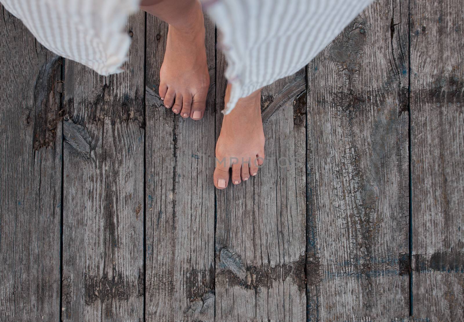 Beautiful female bare bare tanned legs with pink pedicure on wooden beach flooring. Top view, copy space.