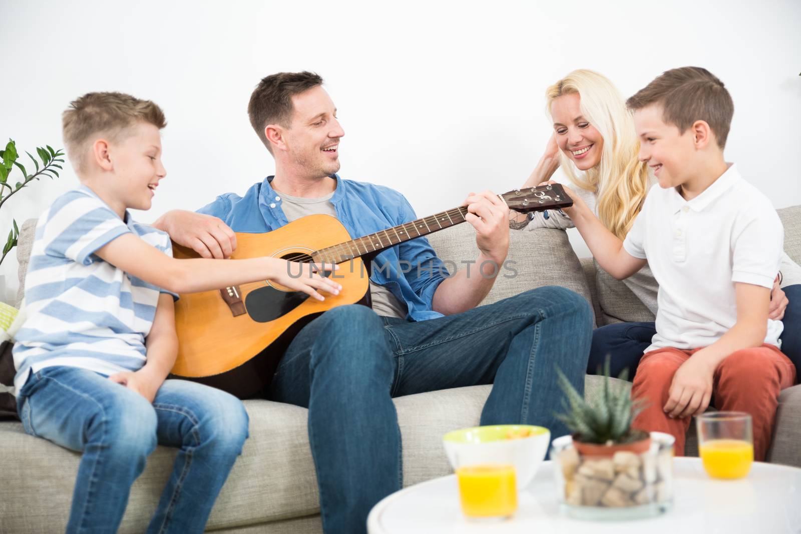 Happy caucasian family smiling while playing guitar and singing songs together at cosy modern home. Spending quality leisure time with children and family concept.