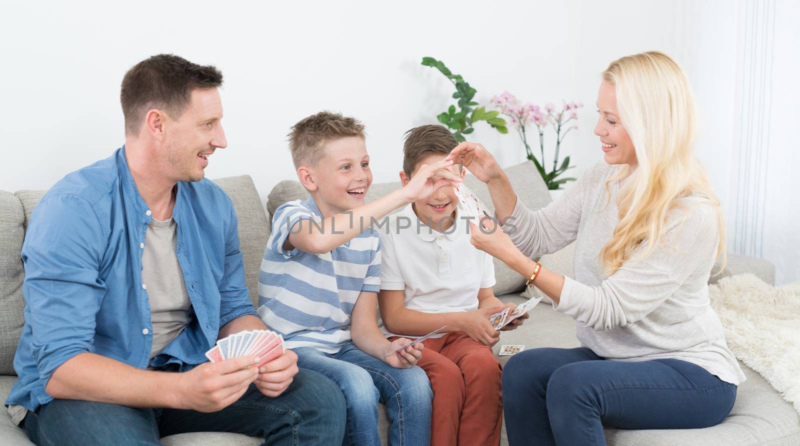 Happy young family playing card game on living room sofa at home. Spending quality leisure time with children and family concept.