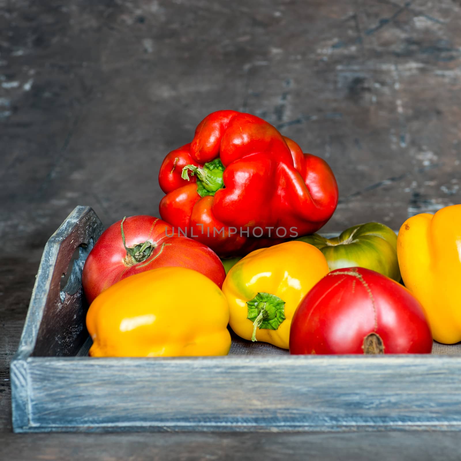 Imperfect natural peppers and tomatoes on an old wooden tray on a dark background. Healthy eating concept. Copy Space.