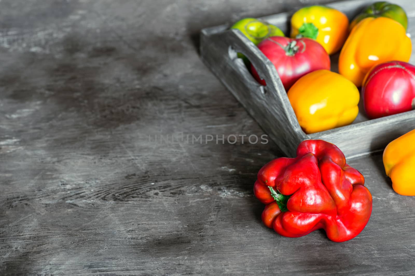 Imperfect natural peppers and tomatoes on an old wooden tray on a dark background. Healthy eating concept. Copy Space.