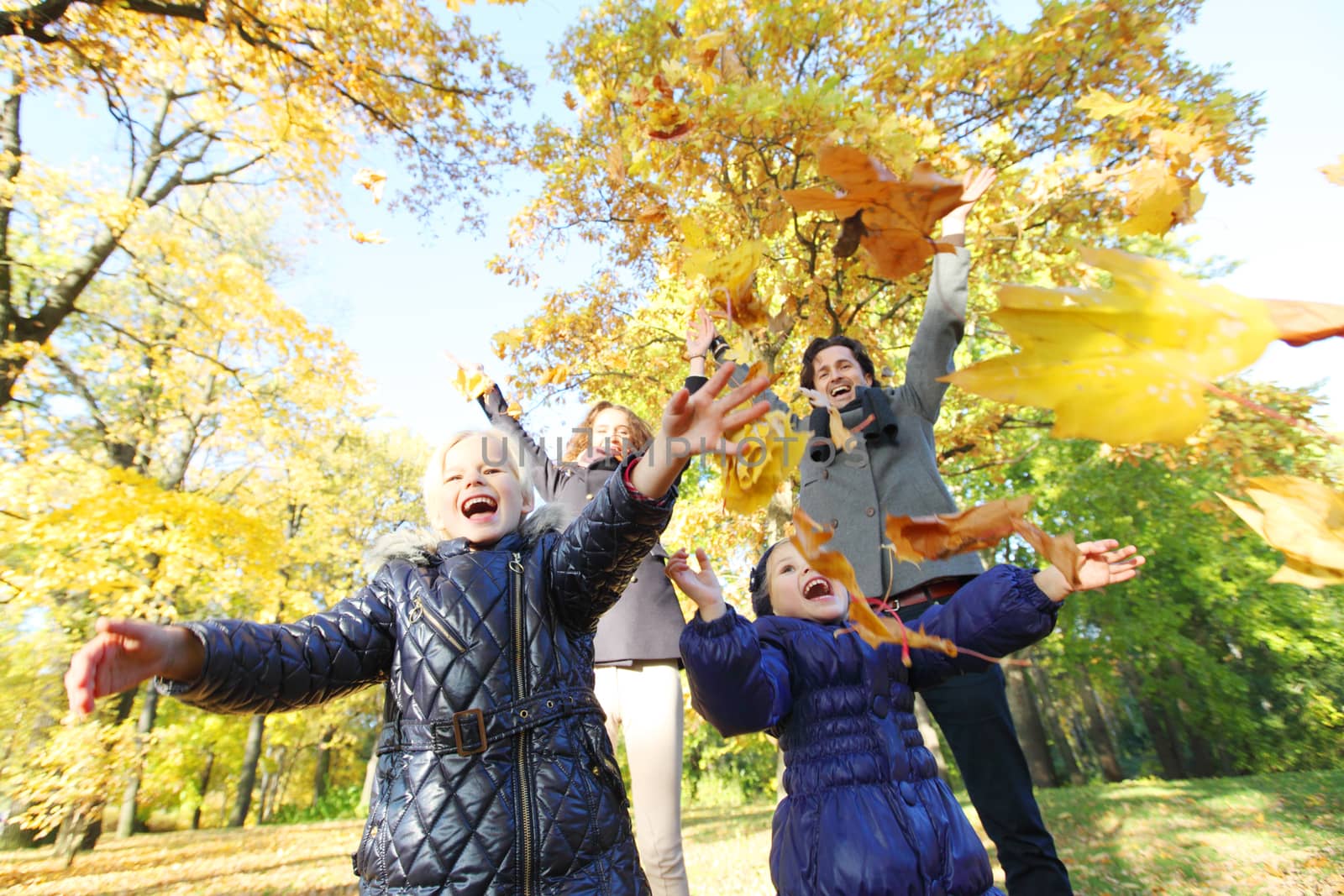 Happy smiling family of parents and children playing throwing leaves in autumn park