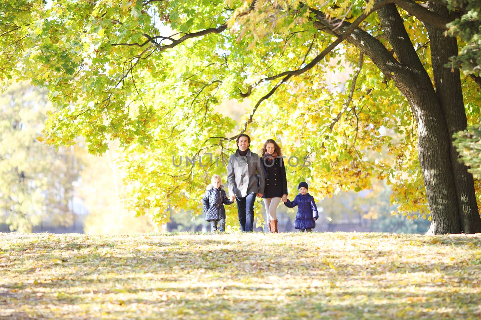 Happy smiling family of parents and children walking together holding hands in autumn park