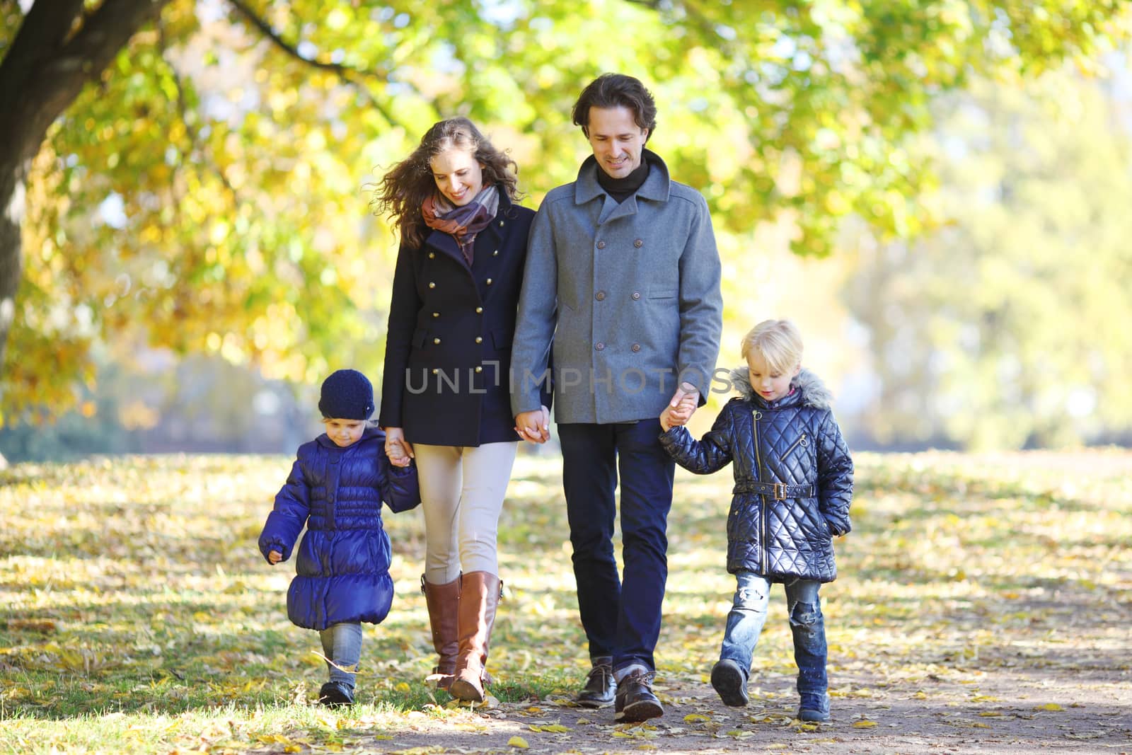 Happy smiling family of parents and children walking together holding hands in autumn park