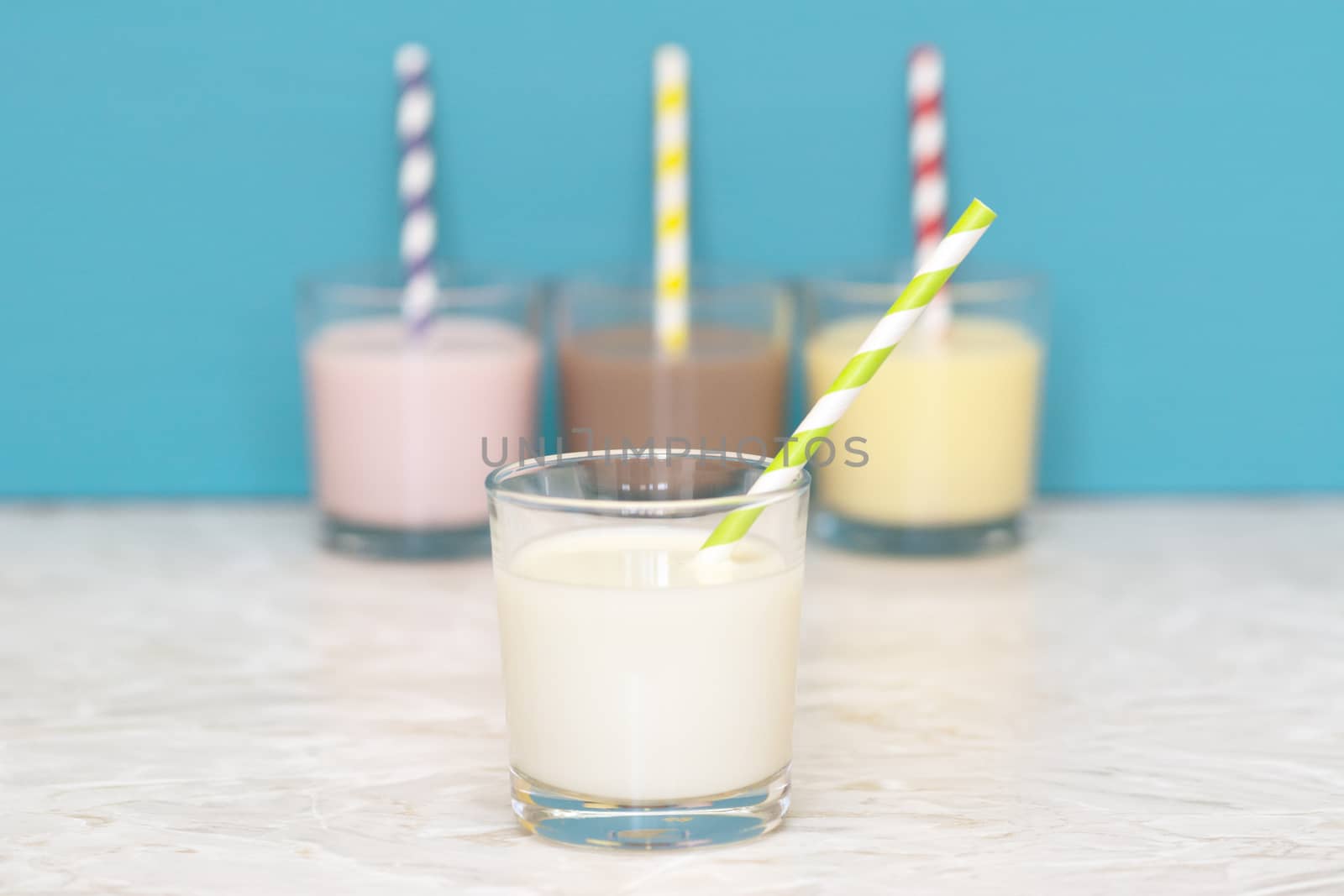Fresh milk with a retro paper straw in front of a row of flavoured milkshakes against a teal background