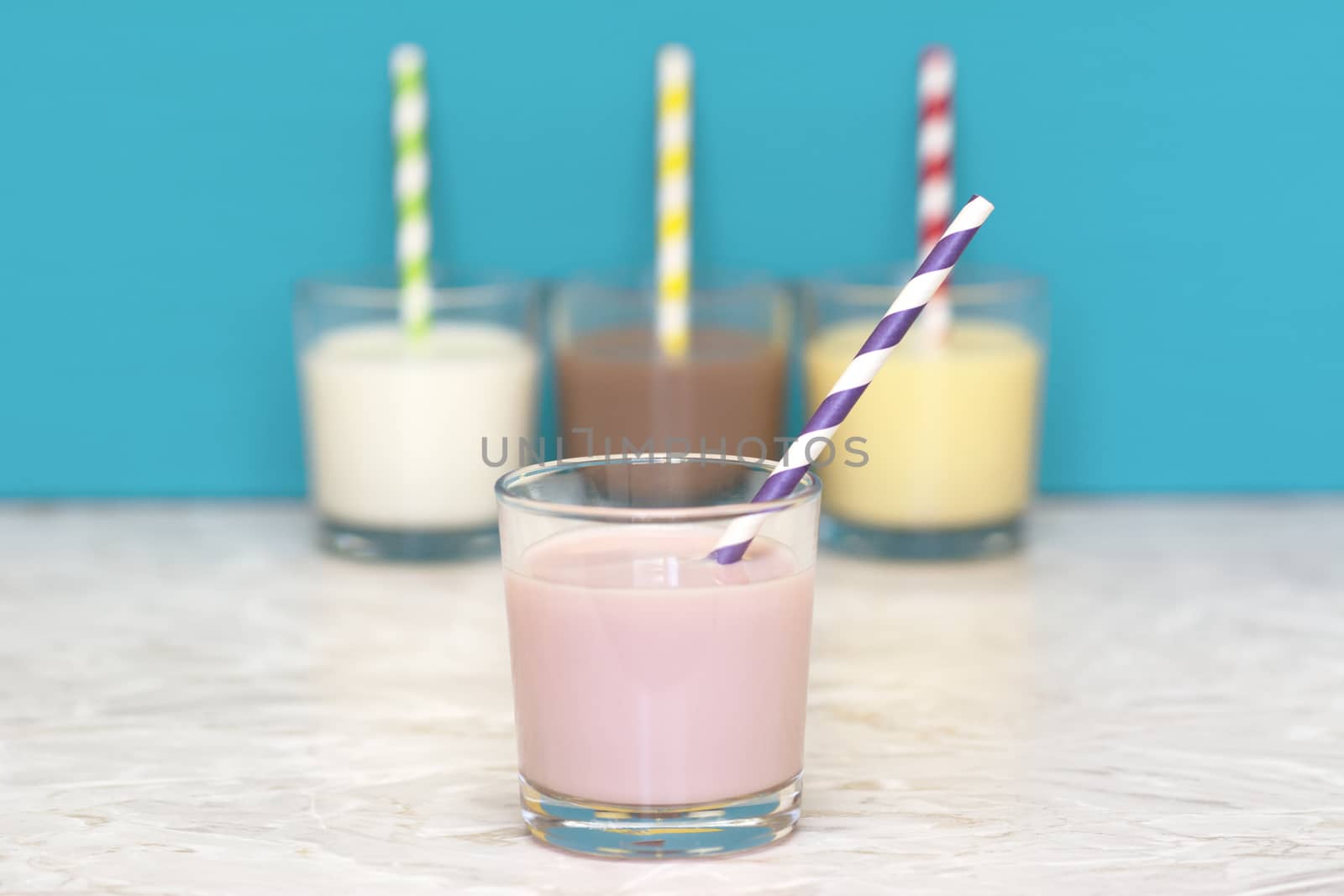 Strawberry milkshake with a retro paper straw in front of a row of fresh milk and flavoured milkshakes against a teal background