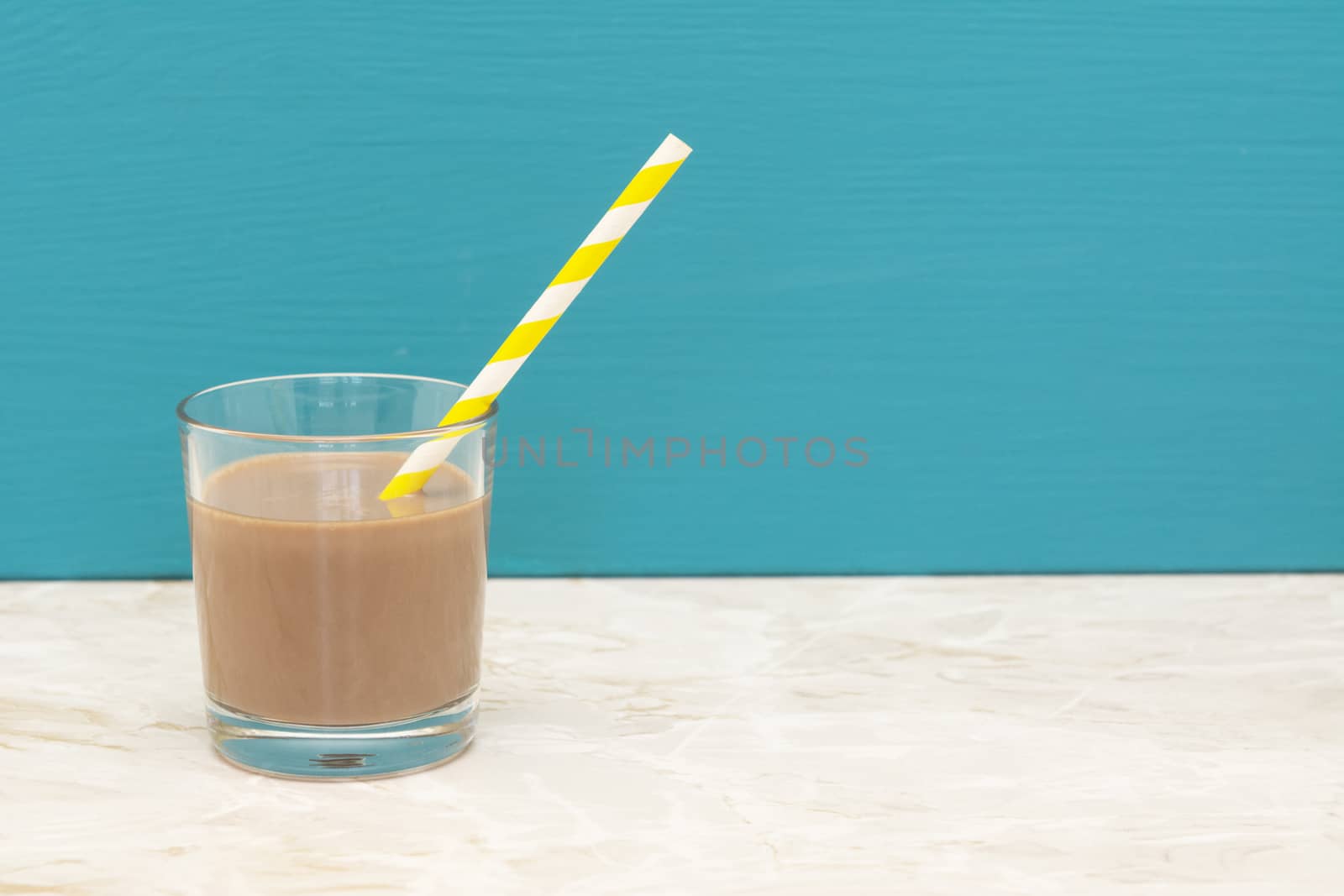 Thick chocolate milkshake with a retro paper straw in a glass tumbler with a teal background and copy space