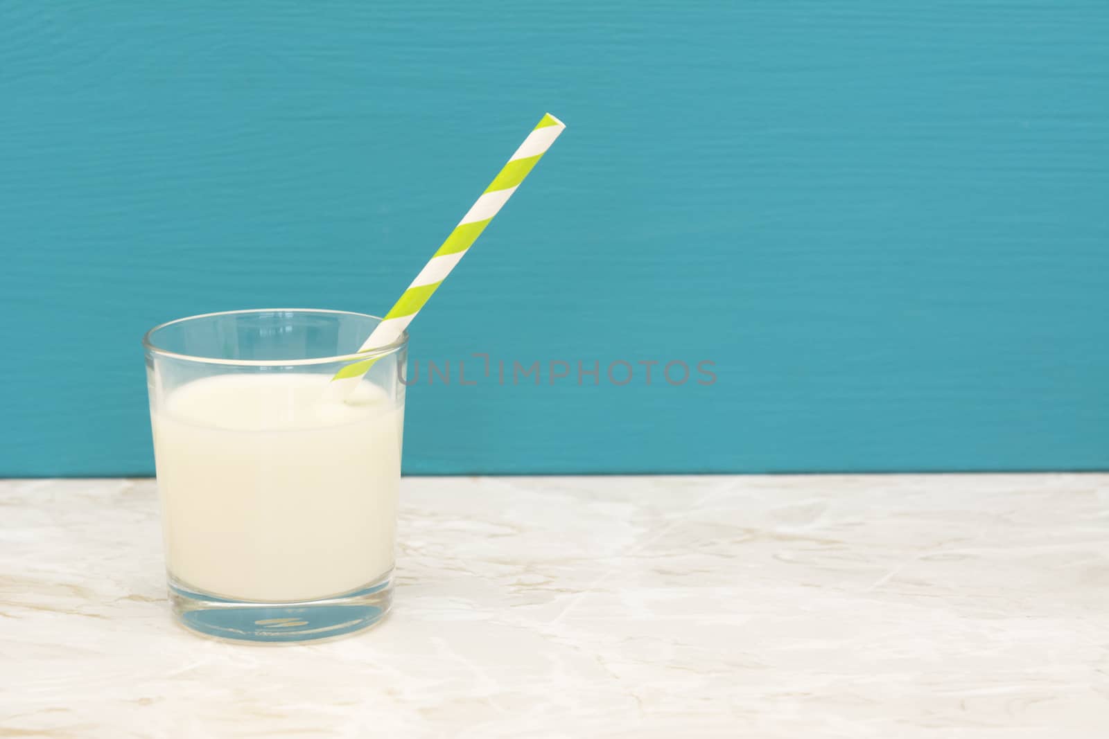 Creamy, fresh milk with a retro paper straw in a glass tumbler with a teal background and copy space