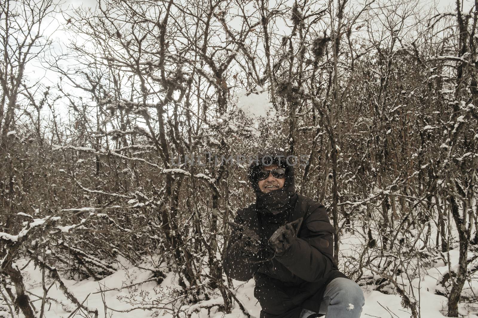 Smiling happy joyful Portrait of a Man wearing a black pullover jacket enjoying first snow playing and throwing snowball in air. Enjoy Snowing day view in winter. Rural village Jammu and Kashmir India by sudiptabhowmick