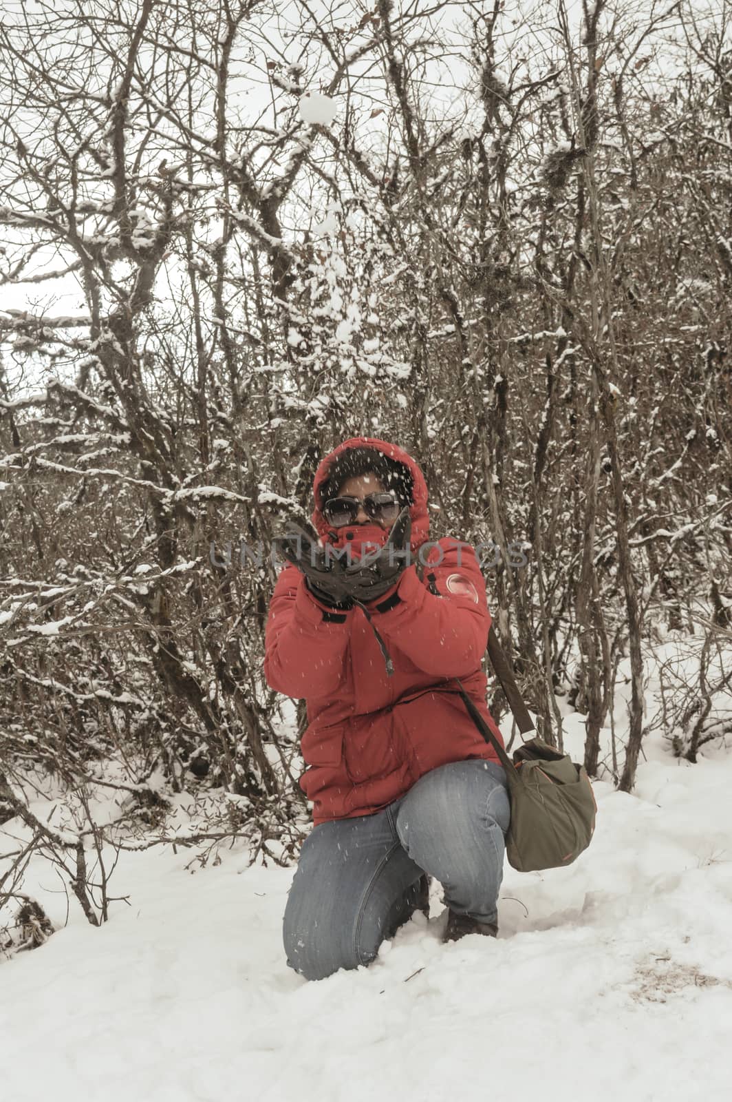 Smiling happy joyful Portrait of a Woman wearing a red pullover jacket enjoying first snow playing and throwing snowball in air. Enjoy Snowing day view in winter. Rural village Jammu and Kashmir India