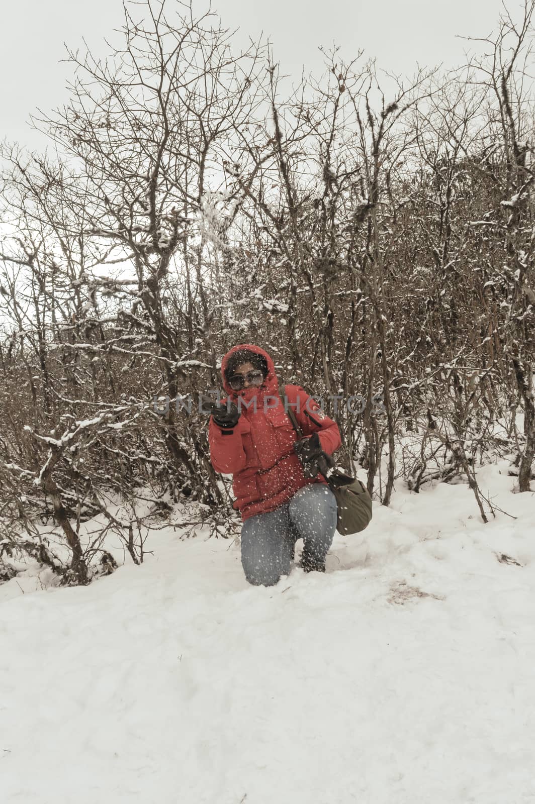 Smiling happy joyful Portrait of a Woman wearing a red pullover jacket enjoying first snow playing and throwing snowball in air. Enjoy Snowing day view in winter. Rural village Jammu and Kashmir India by sudiptabhowmick