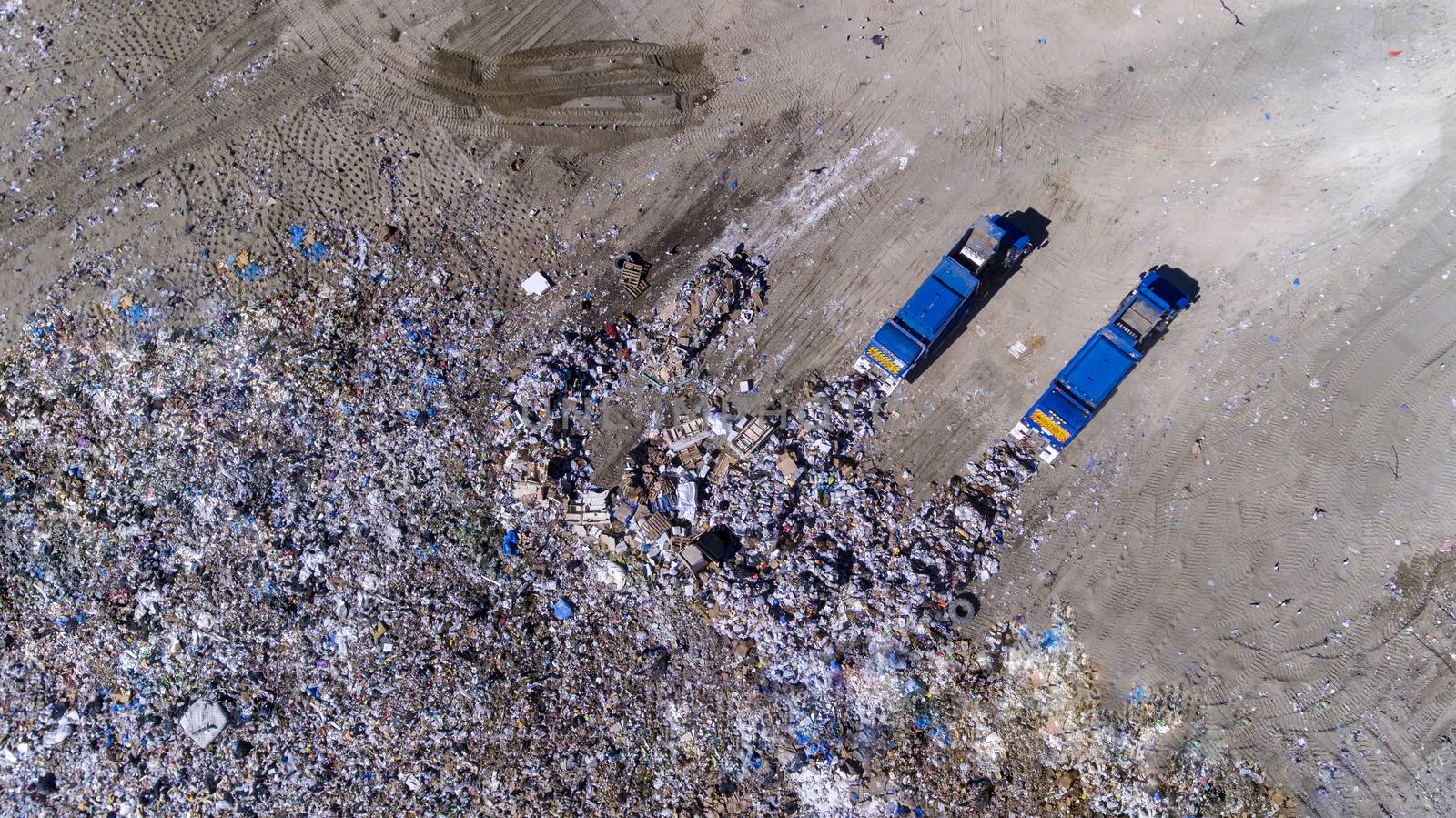 two trash trucks dump waste products polluting our environment in an open landfill