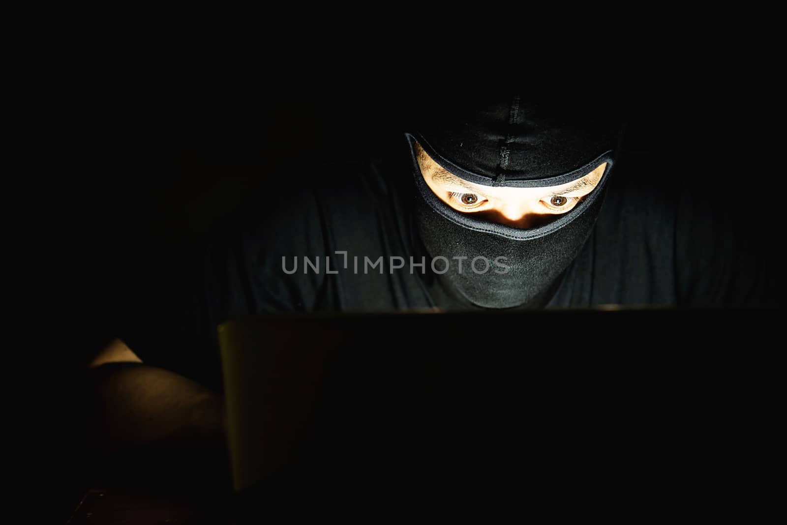Computer hacker doing his job with laptop computer in the dark room - people with computer criminal concept by pairhandmade