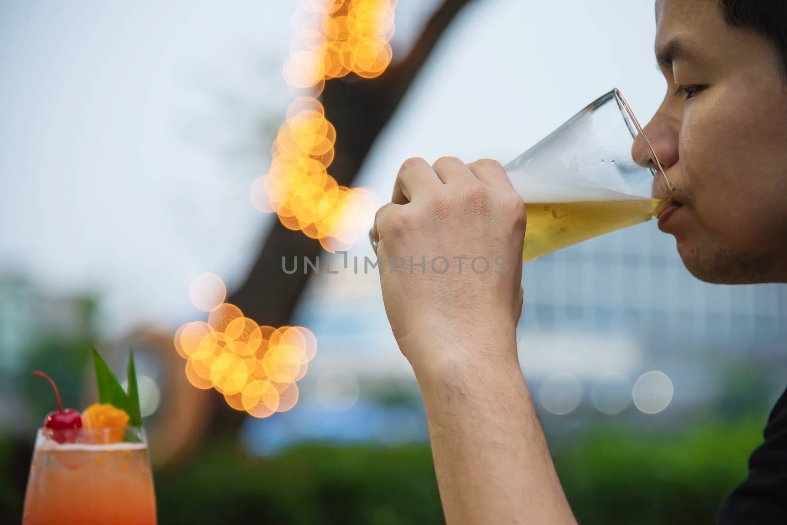 Asian man drinking beer in green garden restaurant - people relax enjoy soft drink lifestyle concept by pairhandmade
