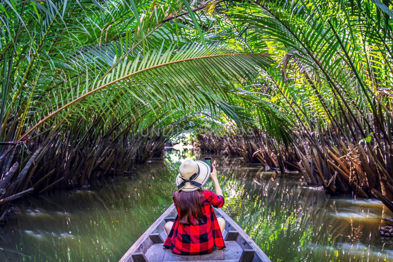 Asian women sitting on a boat at tunnel from nypa fruticans or palm tree in Surat thani,Thailand. by gutarphotoghaphy