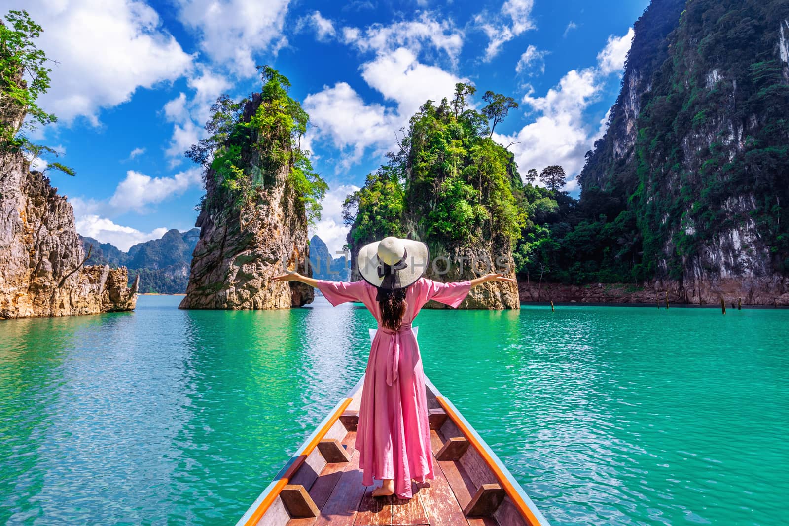 Beautiful girl standing on the boat and looking to mountains in Ratchaprapha Dam at Khao Sok National Park, Surat Thani Province, Thailand. by gutarphotoghaphy