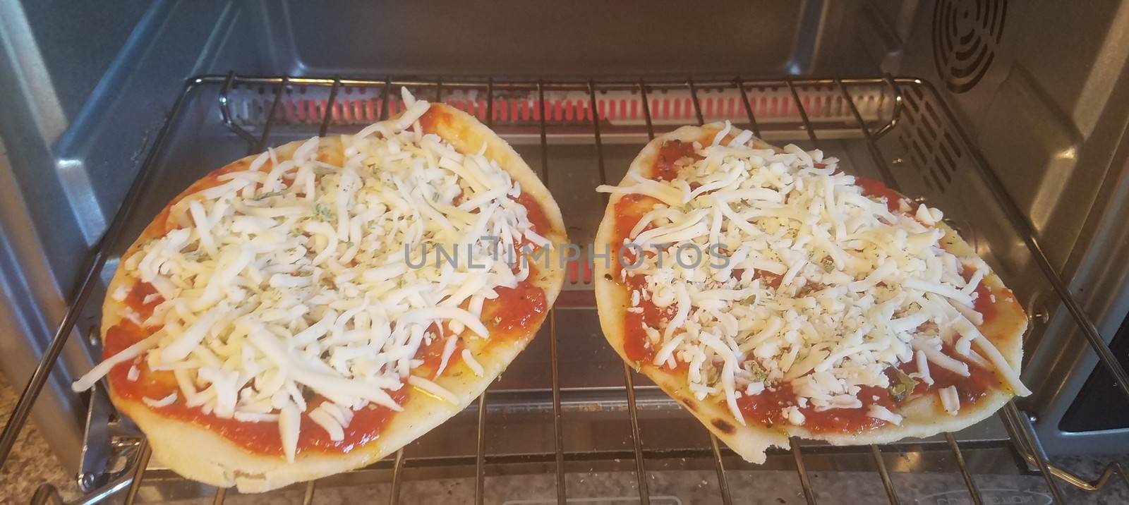 two small pizzas cooking in a toaster oven on a rack