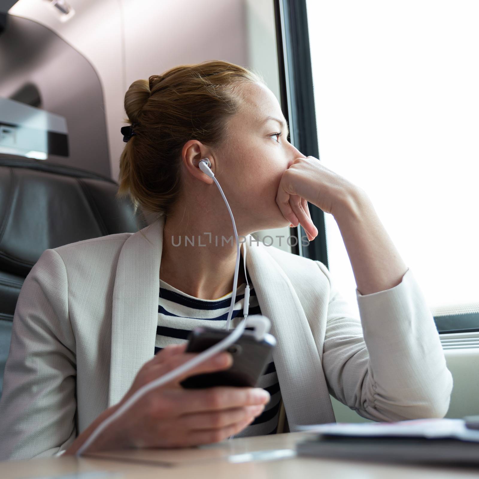 Thoughtful businesswoman listening to podcast on mobile phone while traveling by train. by kasto