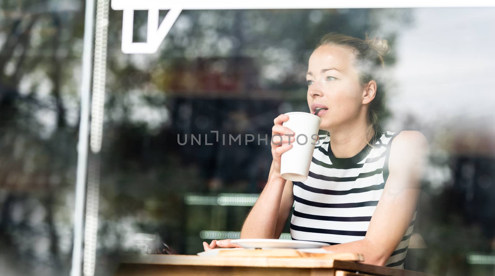 Young caucasian woman sitting alone in coffee shop thoughtfully leaning on her hand, looking trough the window by kasto