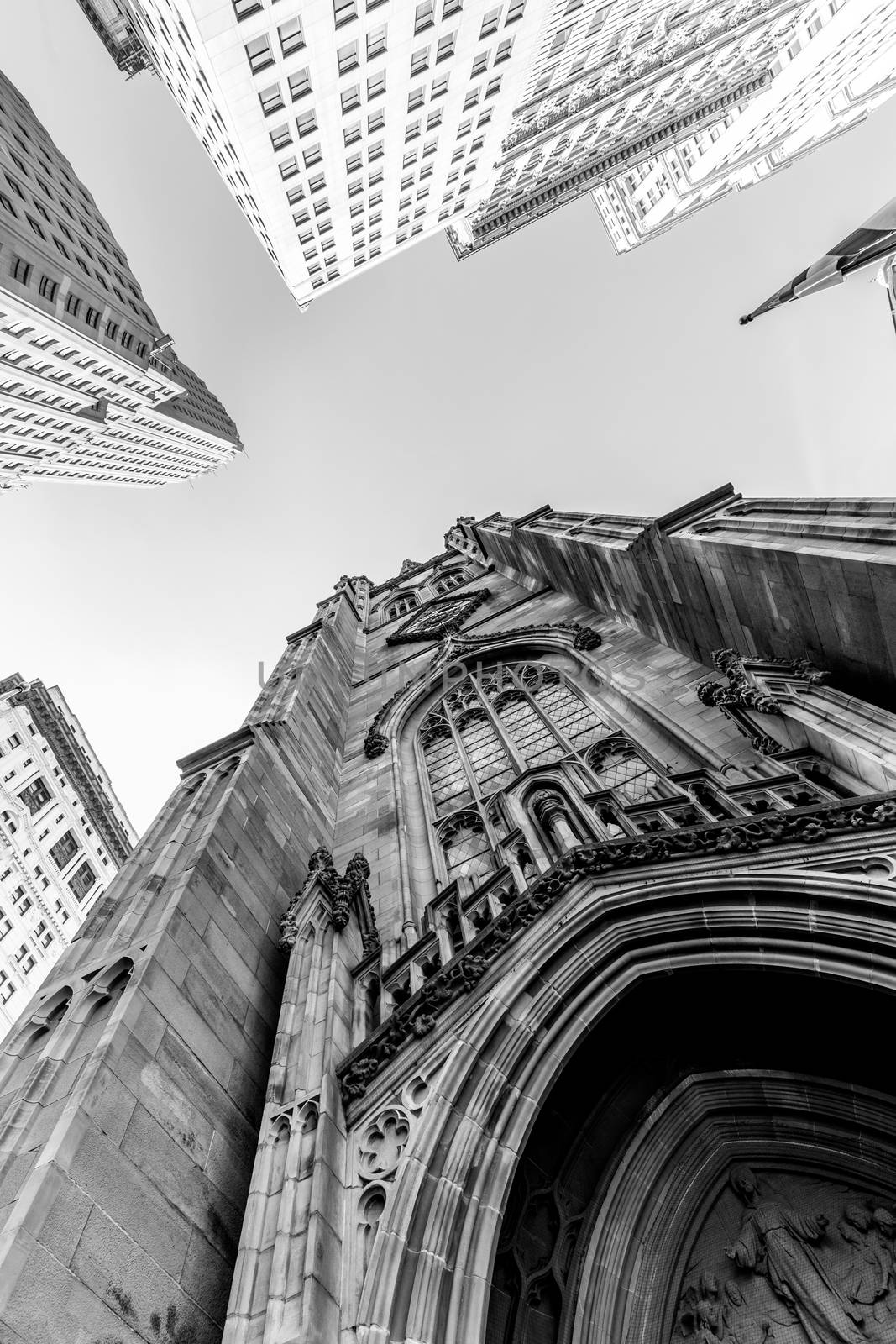 Wide angle upward view of Trinity Church at Broadway and Wall Street with surrounding skyscrapers, Lower Manhattan, New York City, USA. Black and white image.