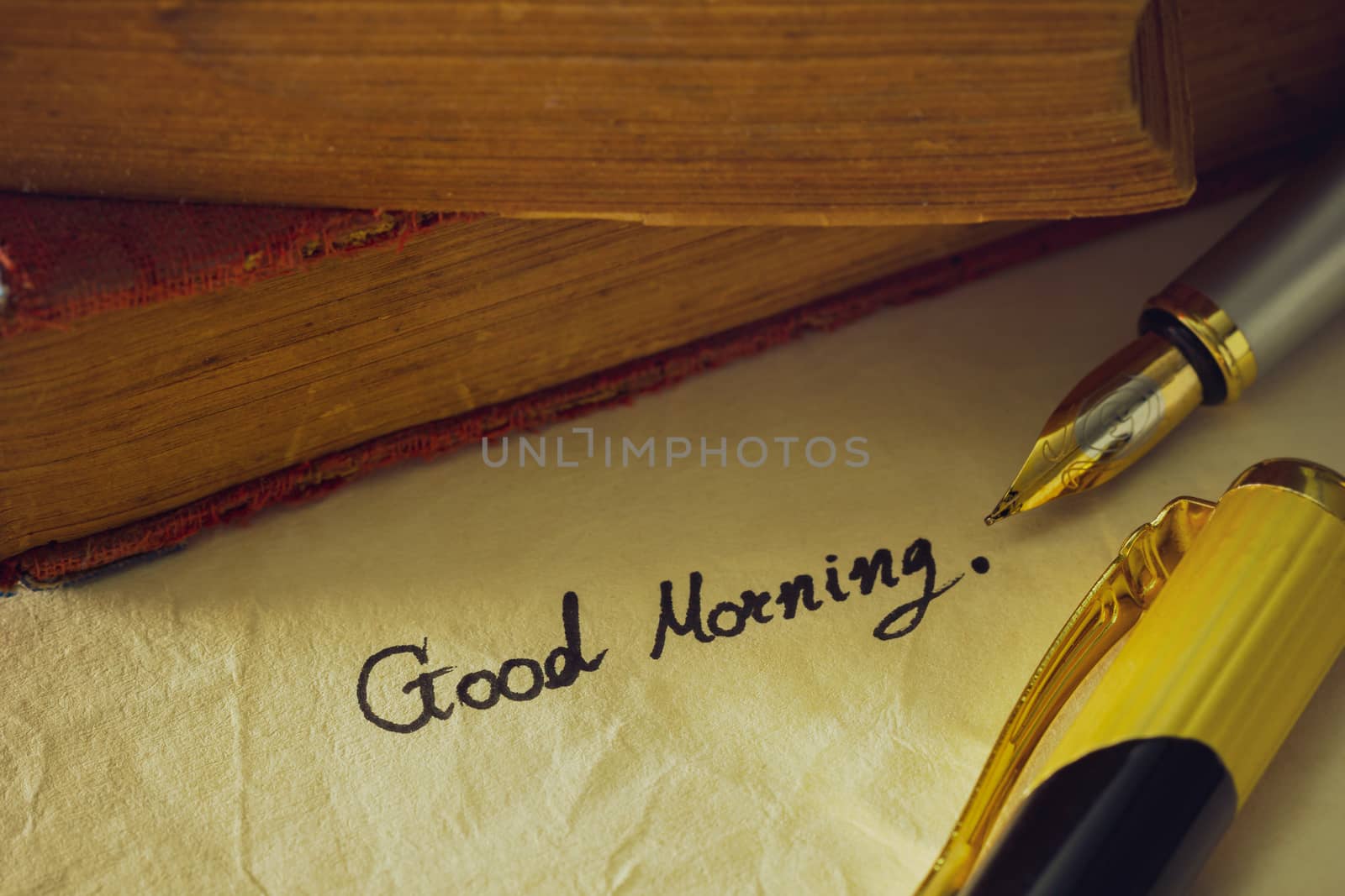 Vintage brass pen writing " Good morning " on old paper and old book stacked on wooden table.