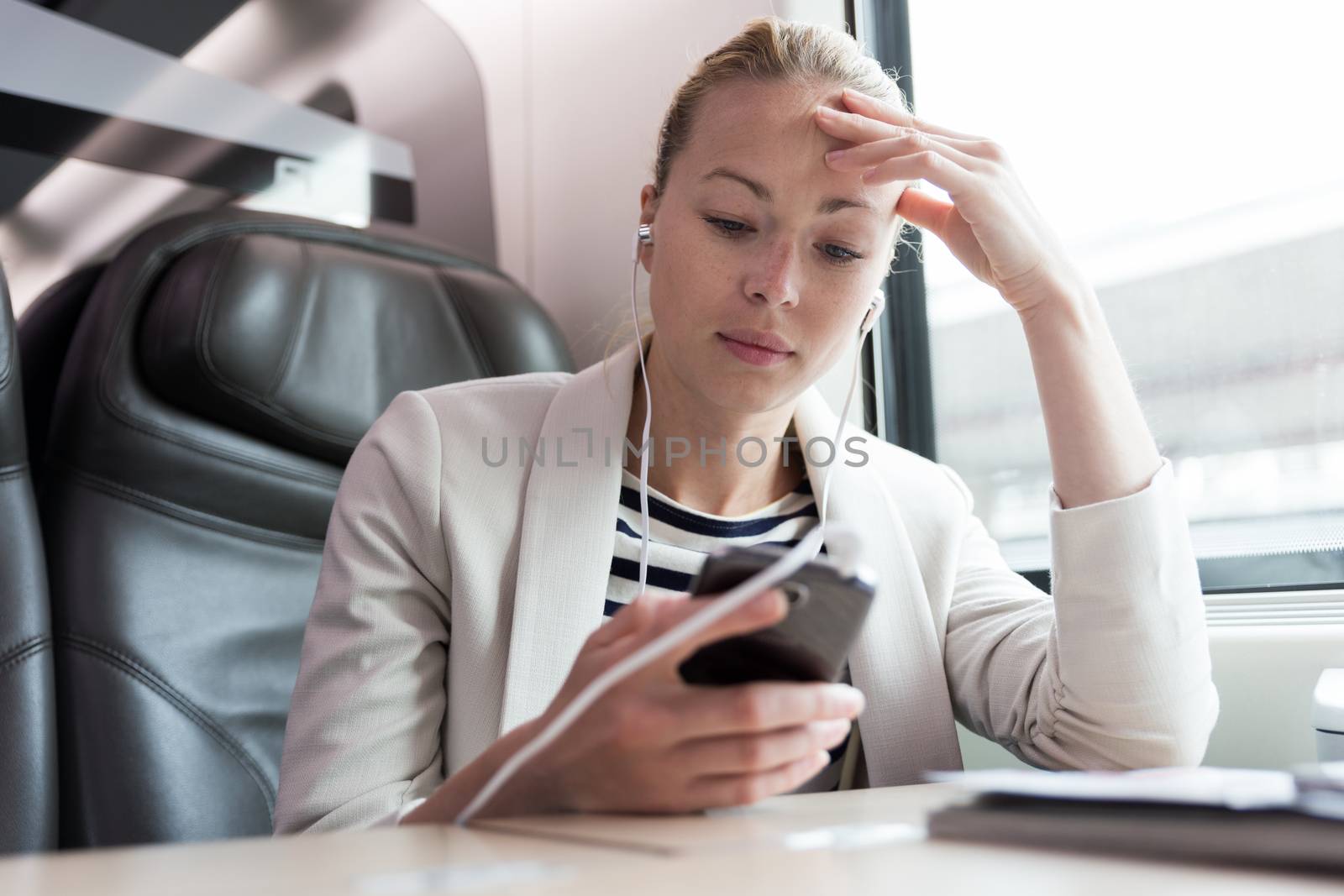 Caucasian businesswoman communicating on cellphone using headphone set while traveling by train in business class seat.