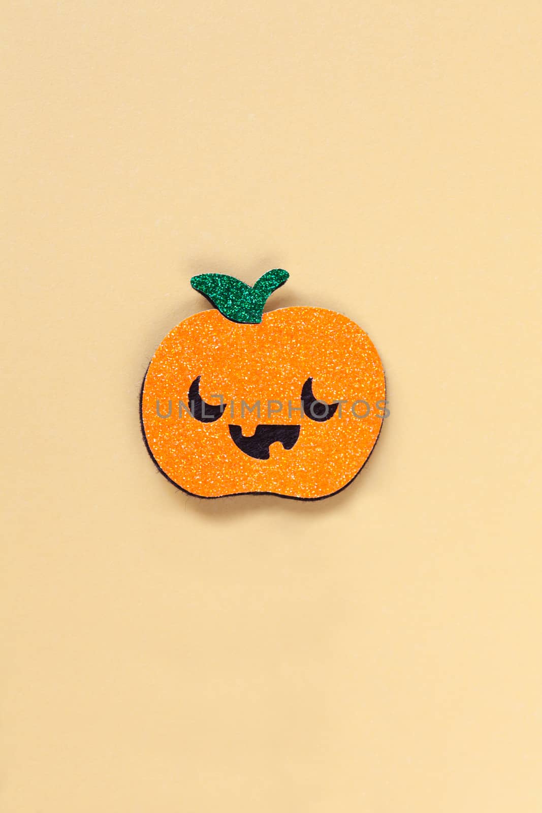 Halloween party accessory, shiny pumpkin with cute creepy faces. Pastel yellow background, place for text. Holiday flat lay. Minimal style. Vertical.