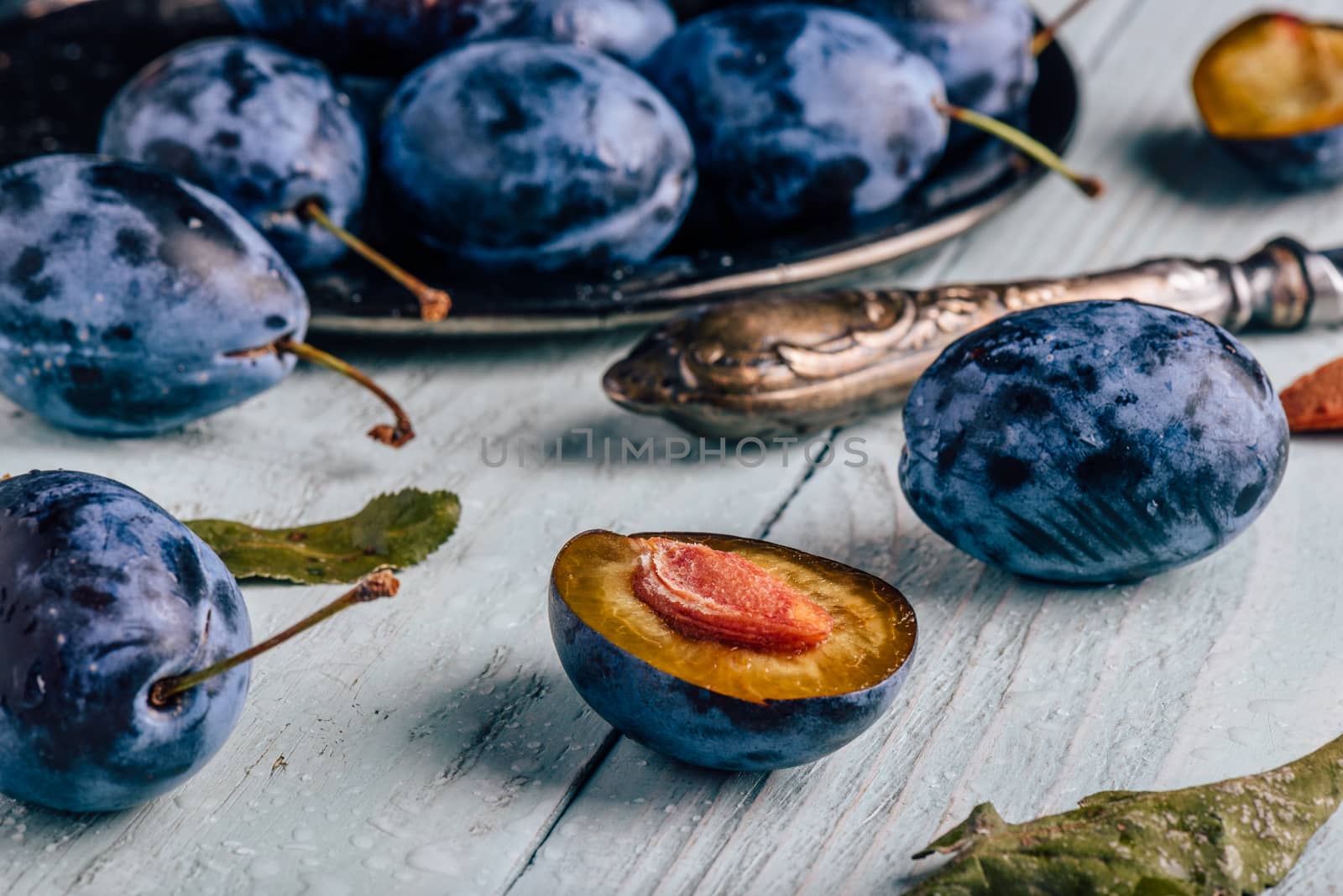 Plums with leaves and knife over wooden surface by Seva_blsv