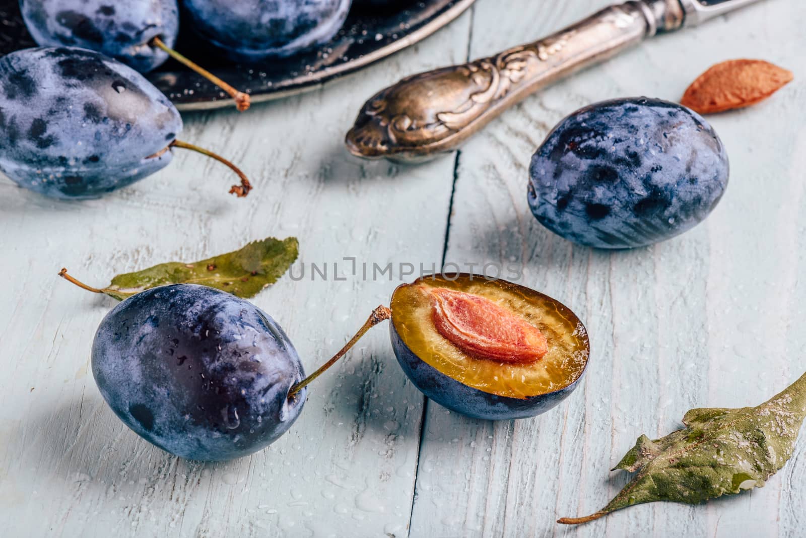 Ripe plums with sliced fruits, leaves and vintage knife over light wooden surface