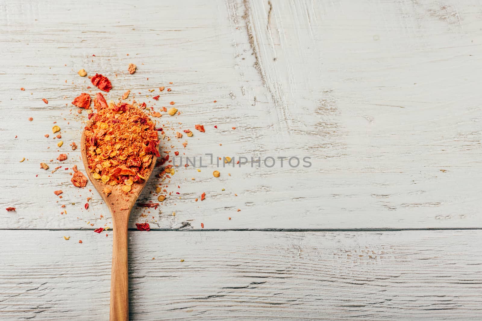 Spoonful of crushed red chili pepper over wooden background