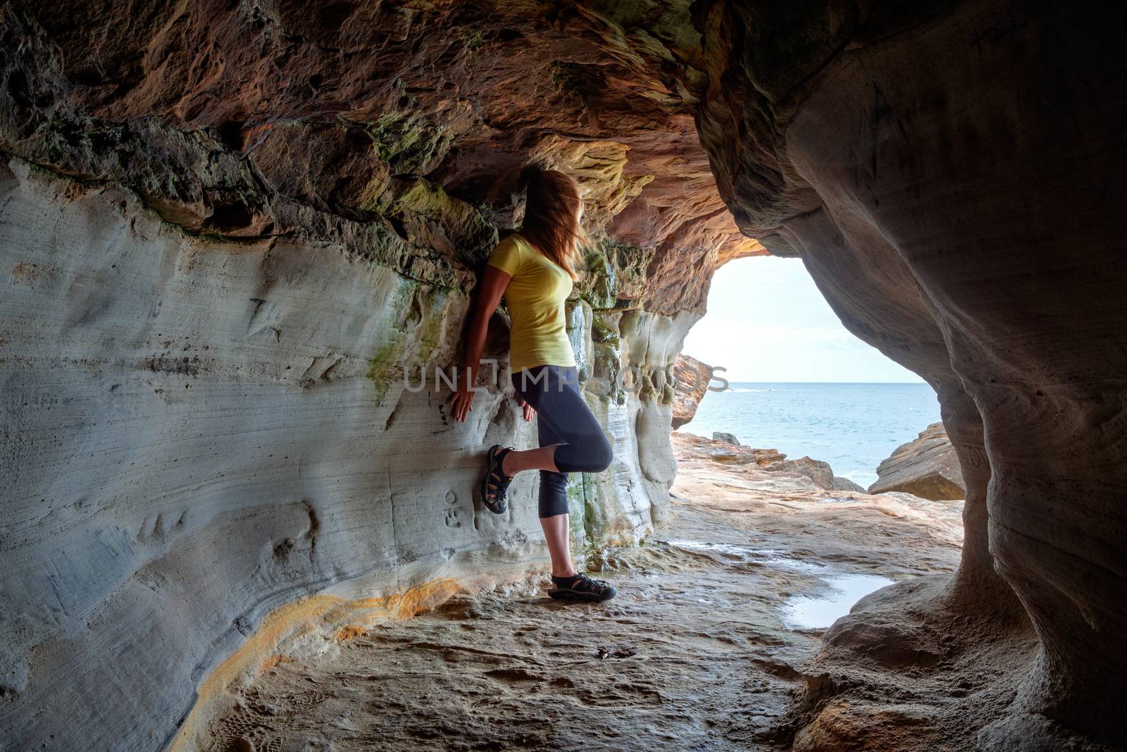 A woman stands in a carved out tunnel that leads to a rock ledge overlooking the ocean