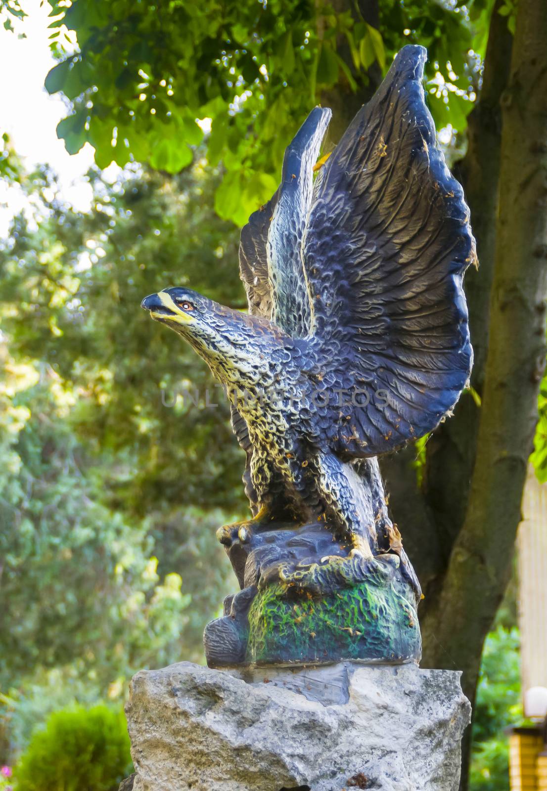 Eagle of granite sitting with his wings spread against the trees.