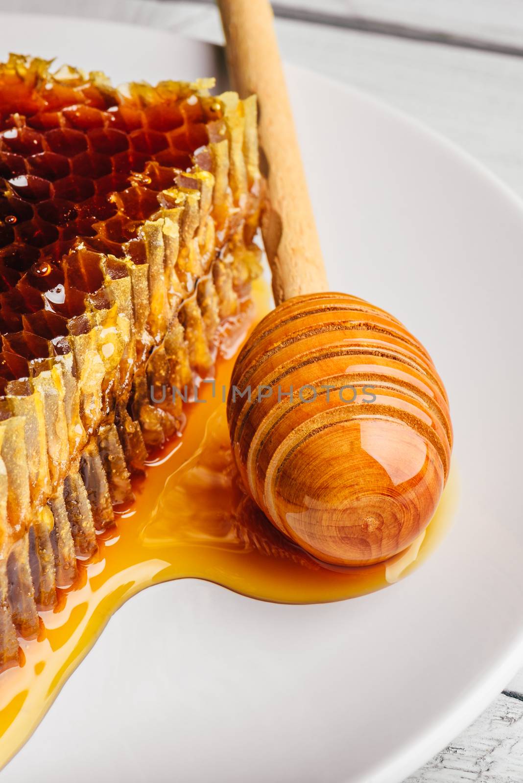 Delicious honeycomb on white plate with wooden honey dipper
