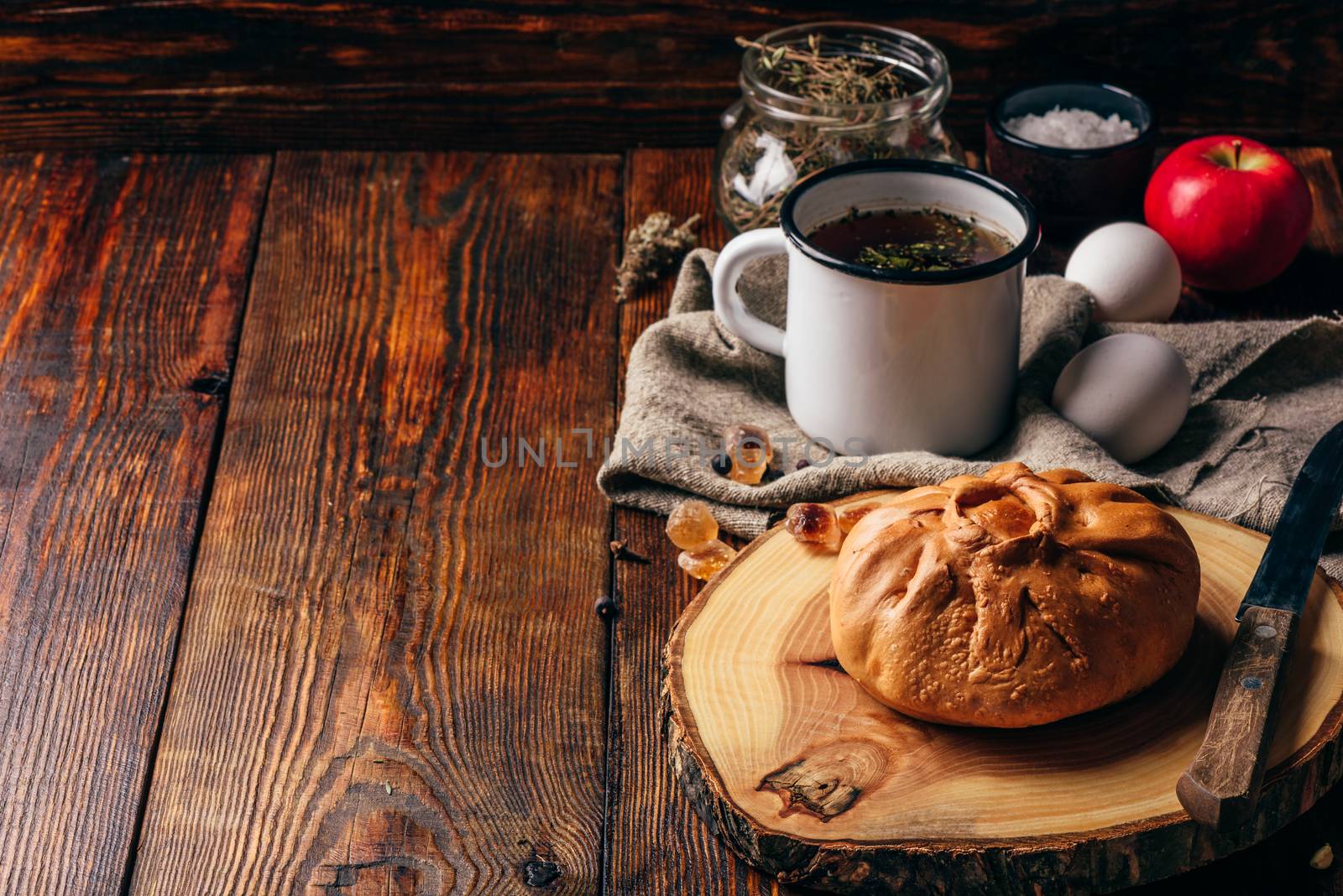 Rustic breakfast with traditional tatar pastry elesh, herbal tea in metal mug, apple and boiled eggs over dark wooden surface