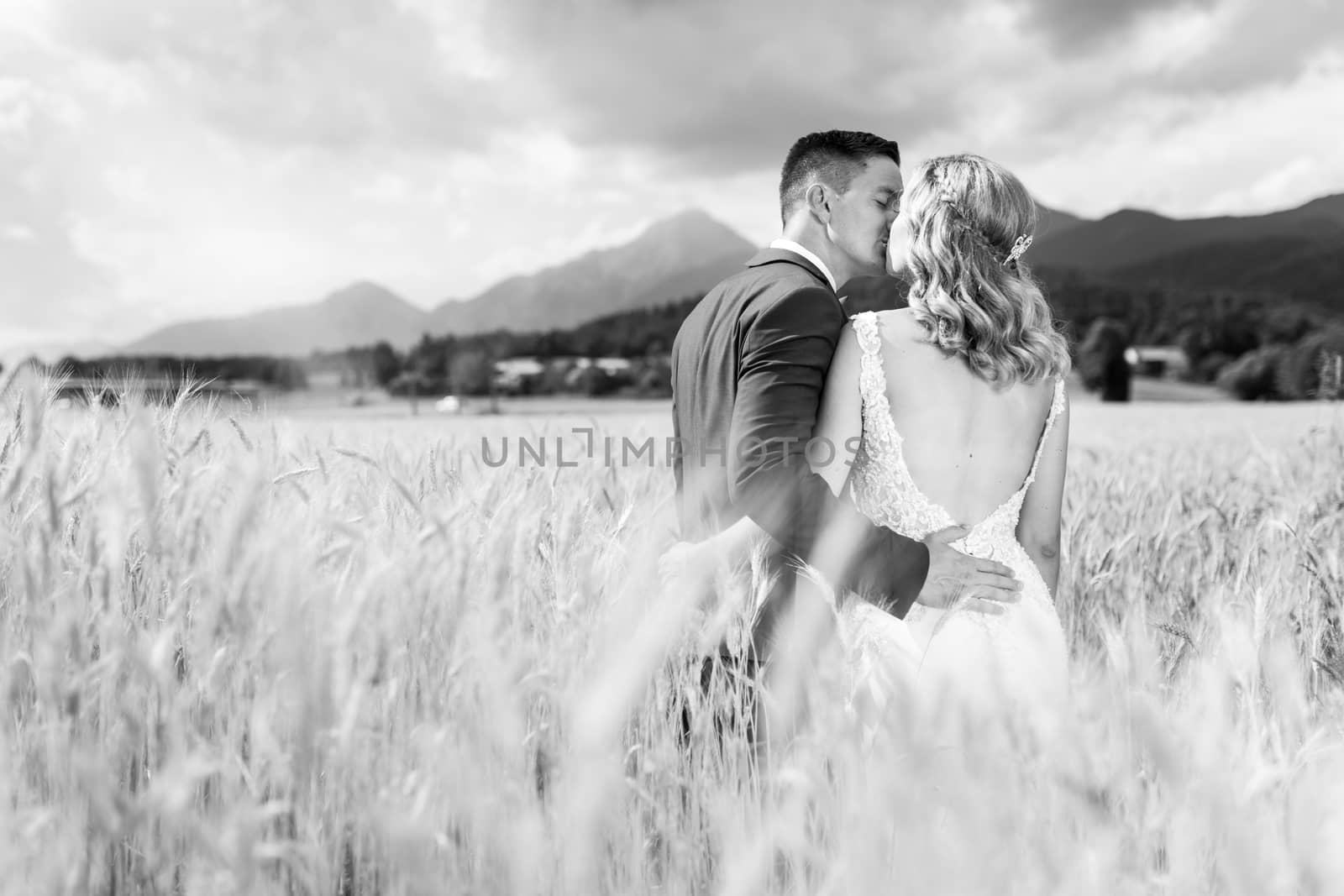 Bride and groom kissing and hugging tenderly in wheat field somewhere in countryside in Slovenia. Caucasian happy romantic young couple celebrating their marriage. Black and white photo.