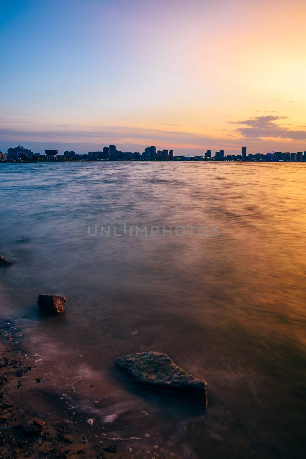 Sunrise view of city with stones in water on foreground