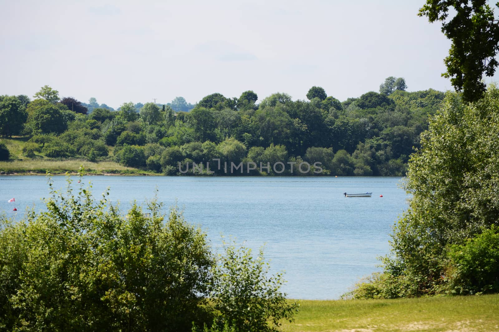 Small boat on Bewl Water reservoir in Tunbridge Wells, Kent. Verdant trees and bushes grow at the water's edge.