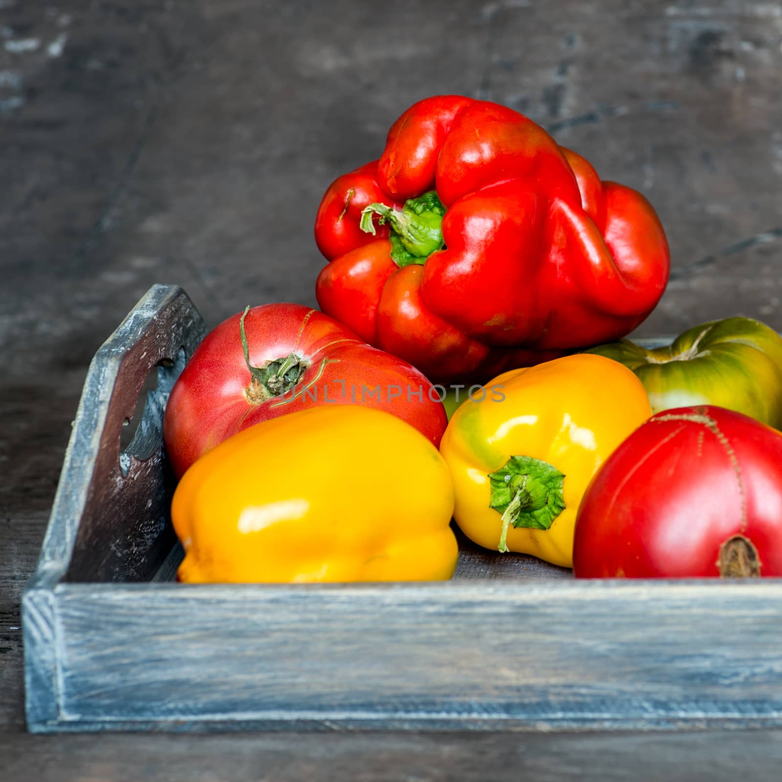 Imperfect natural peppers and tomatoes on an old wooden tray on a dark background. Healthy eating concept