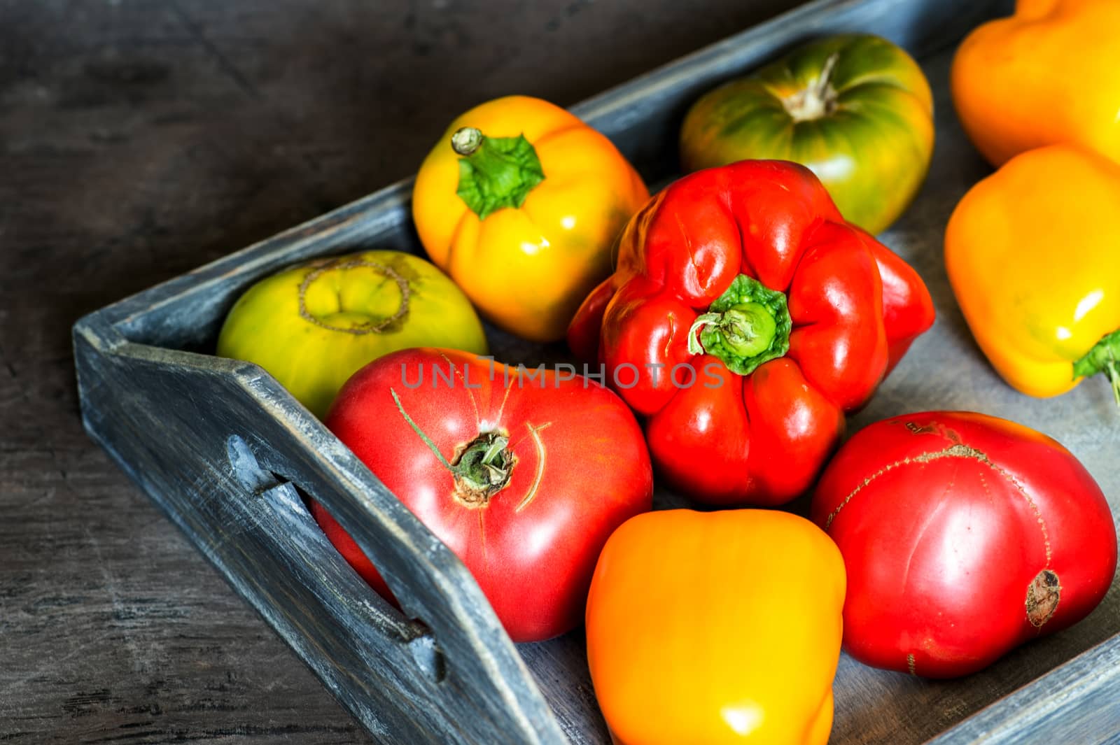 Imperfect natural peppers and tomatoes on an old wooden tray on a dark background. Healthy eating concept