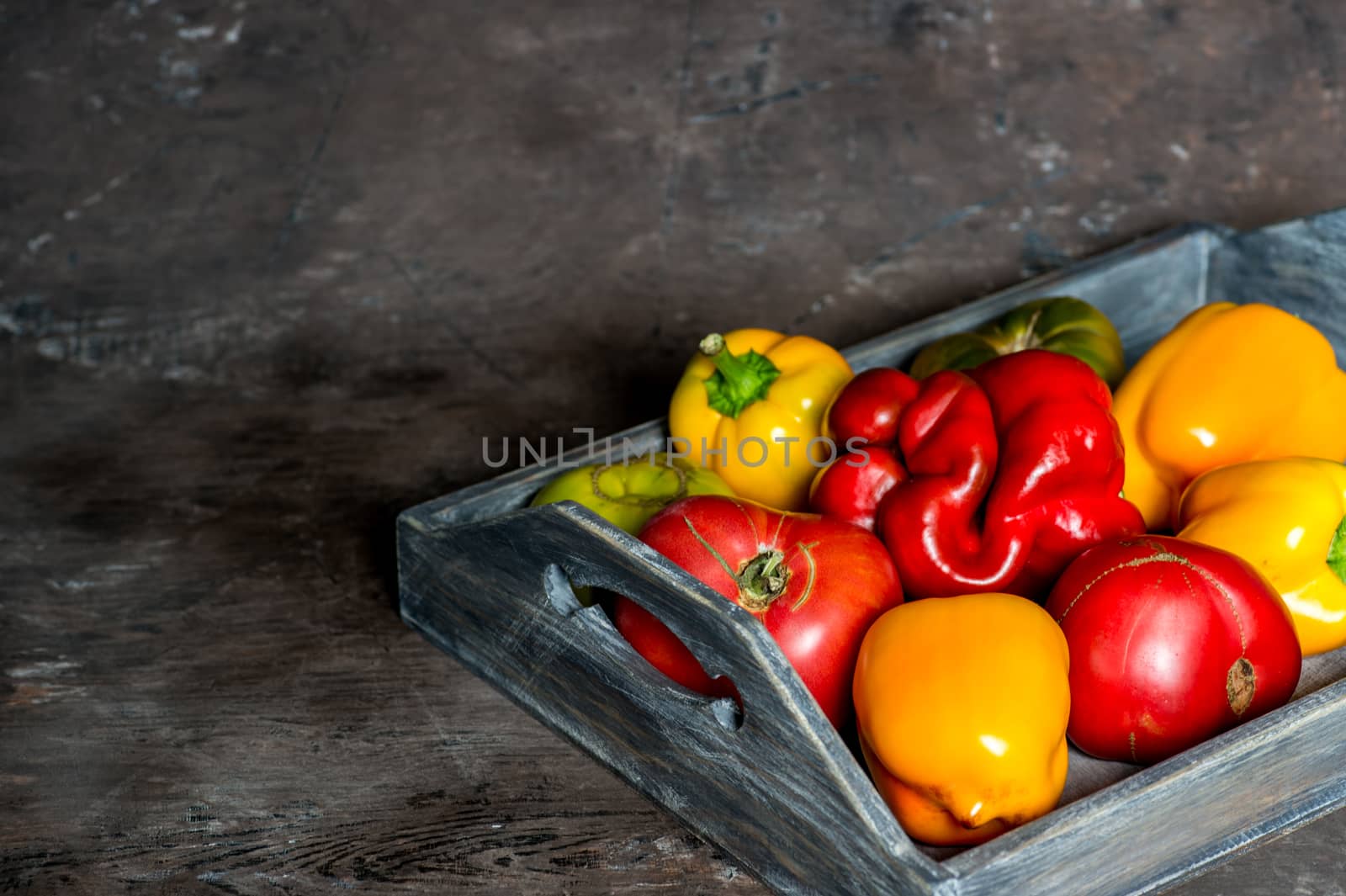 Imperfect natural peppers and tomatoes on an old wooden tray on a dark background. Healthy eating concept. Copy Space.