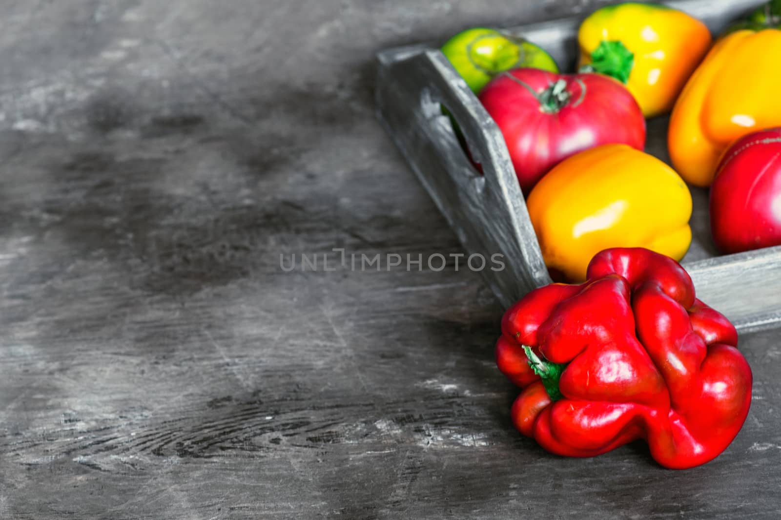 Imperfect natural peppers and tomatoes on an old wooden tray on a dark background. Healthy eating concept. Copy Space.