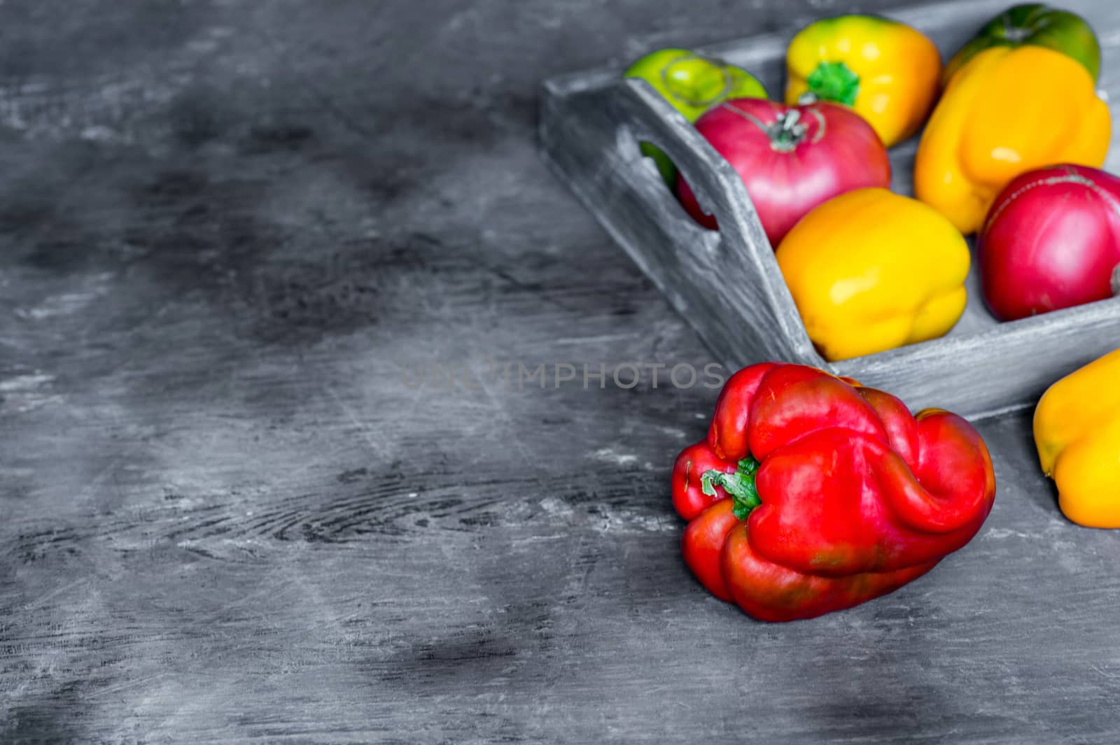 Imperfect natural peppers and tomatoes on an old wooden tray on a dark background. Healthy eating concept. Copy Space.