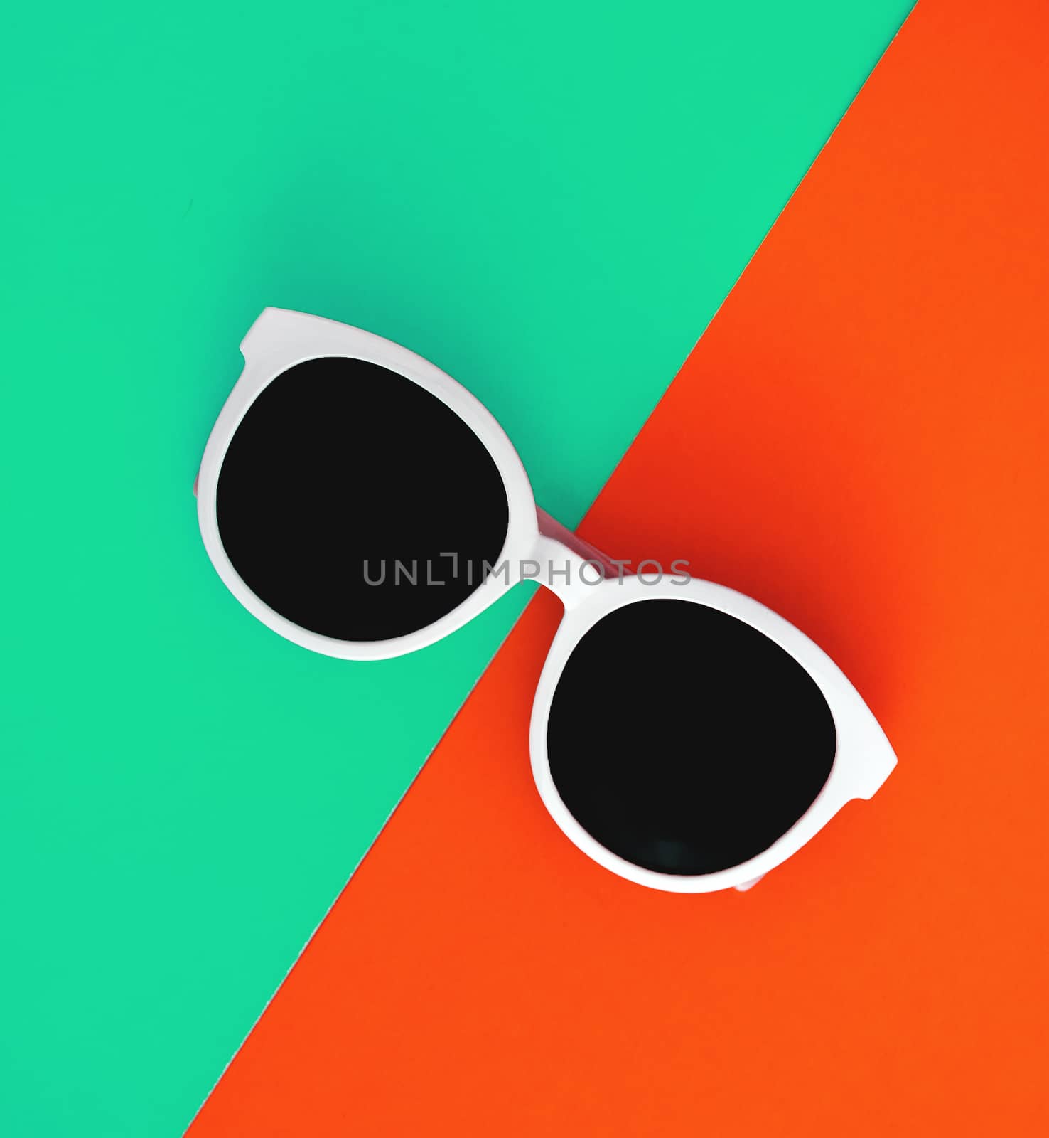 Sunny stylish white sunglasses on a bright blue-cyan and red-orange background, top view, isolated. Copy space. Flat lay by Tanacha