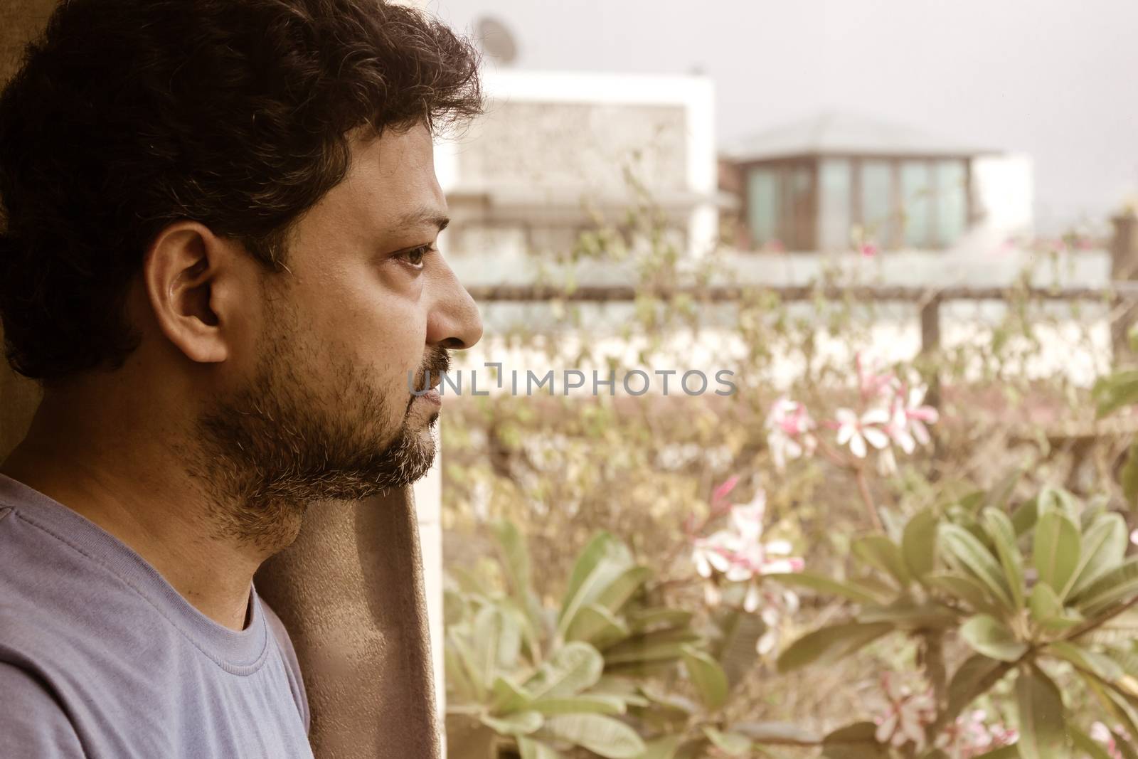 Thoughtful man standing against a window glass staring out in morning with a serious expression. Emotional man looking through window. He is worried, depressed, thoughtful and lonely. waiting concept.