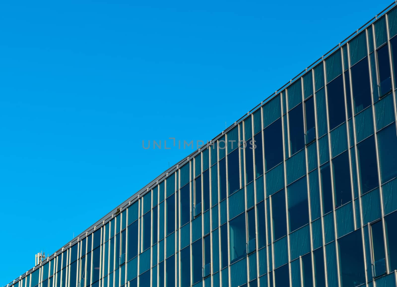 Upper part of modern glass office building diagonally, blue sky in the background.