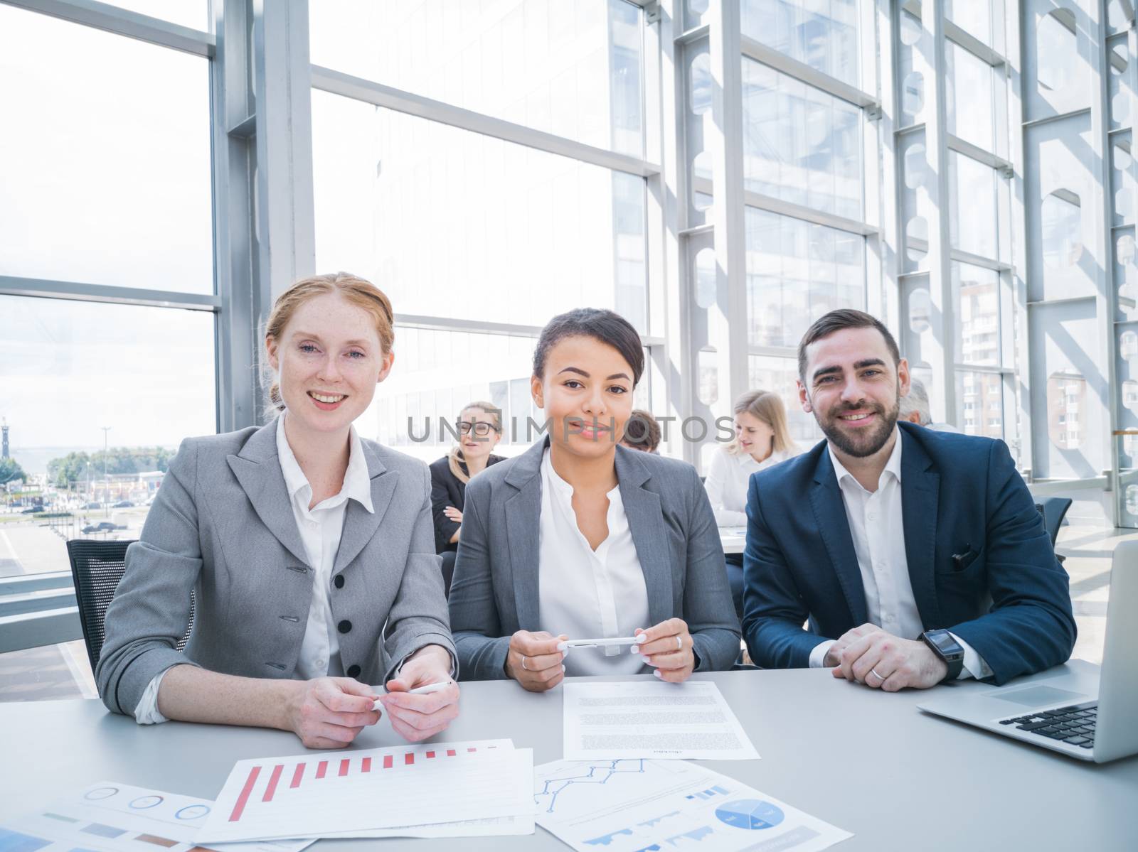 Three smiling business people at conference table with reports. Business meeting and communication concept