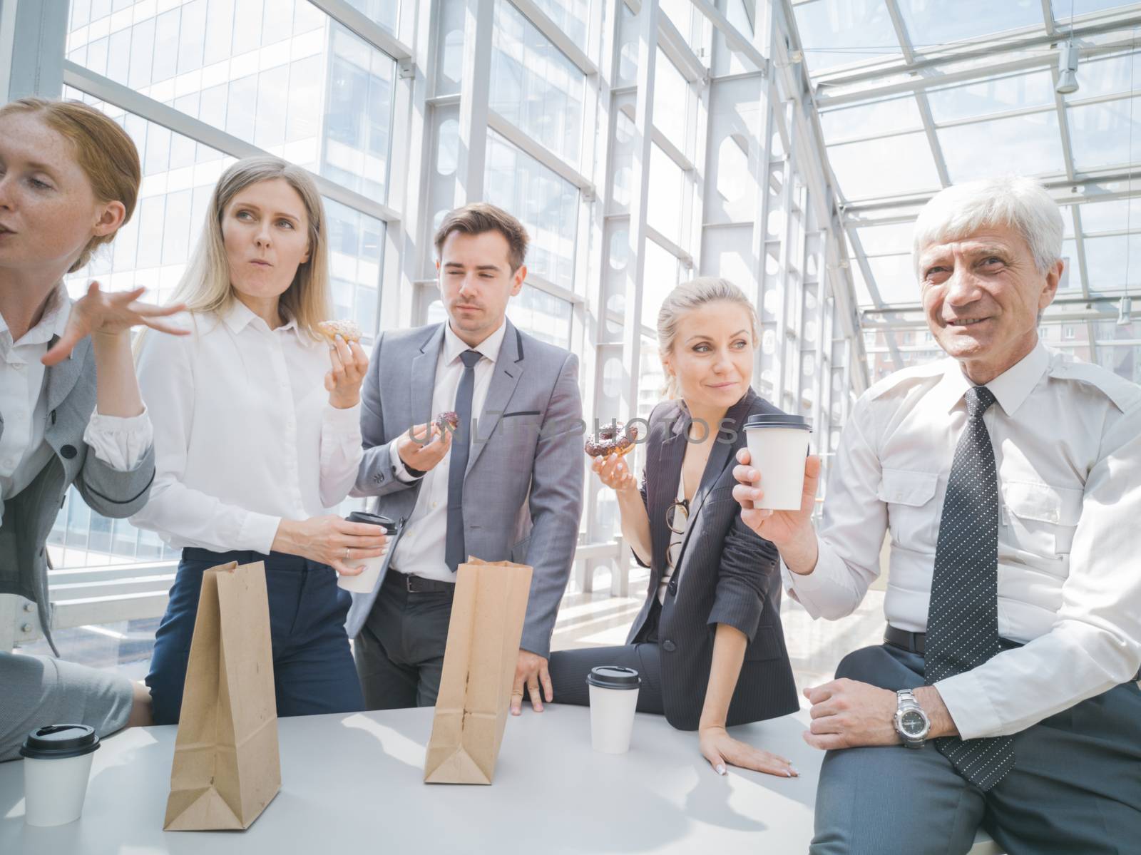 Business people having coffee break eating donuts together in office