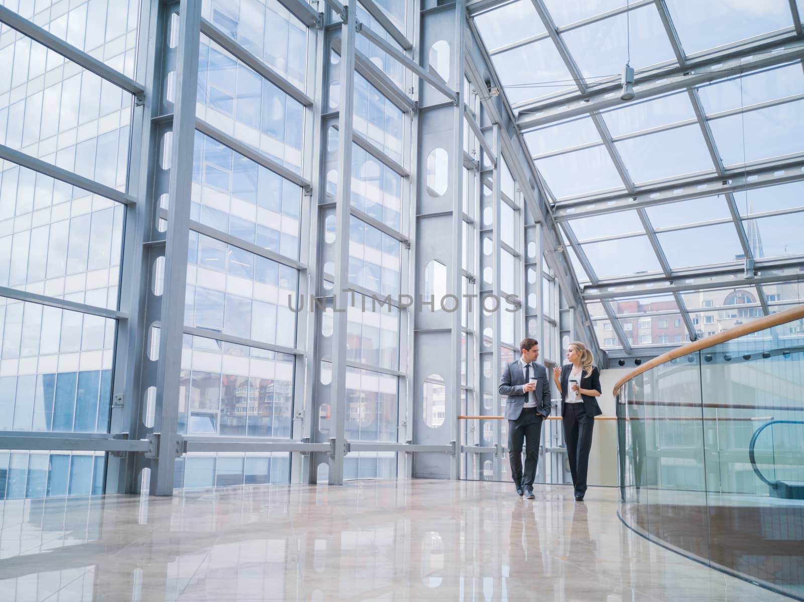 Businessman and businesswoman walk together and talk about business holding coffee in hand