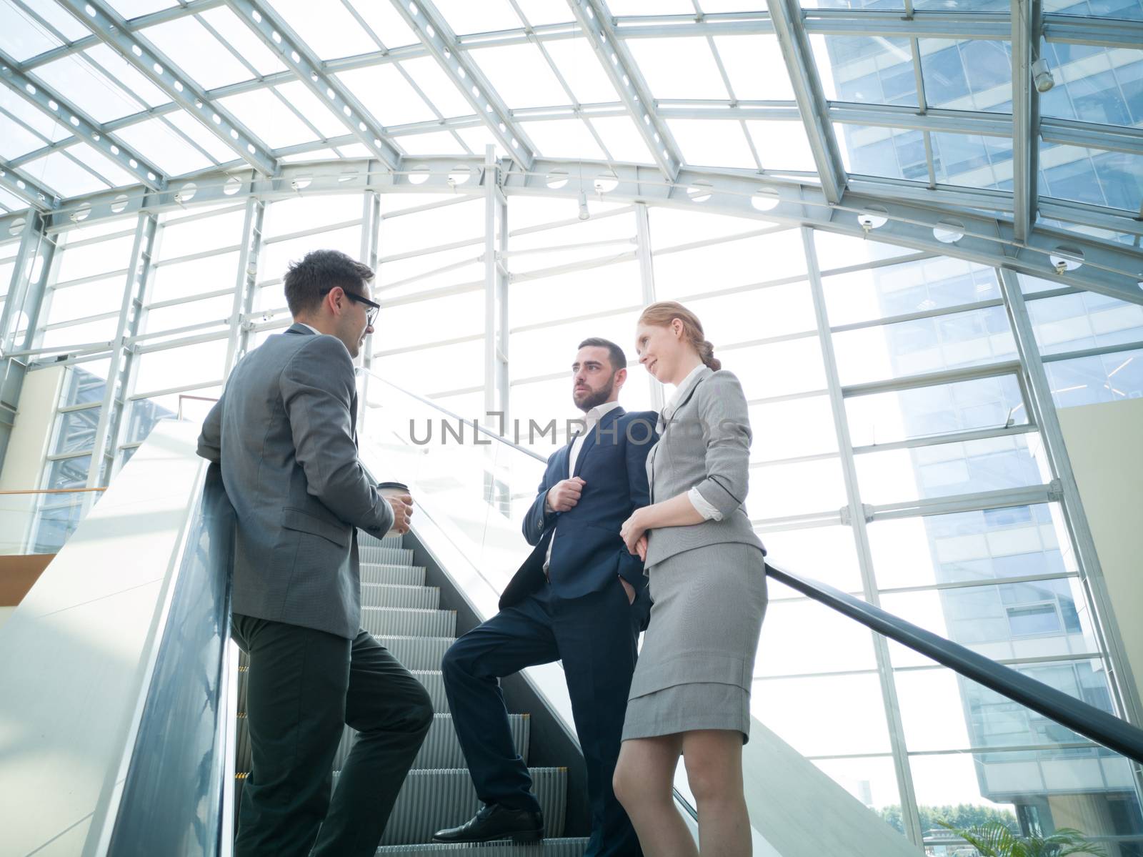 Business people team standing together on escalator and talk about business holding coffee in hand